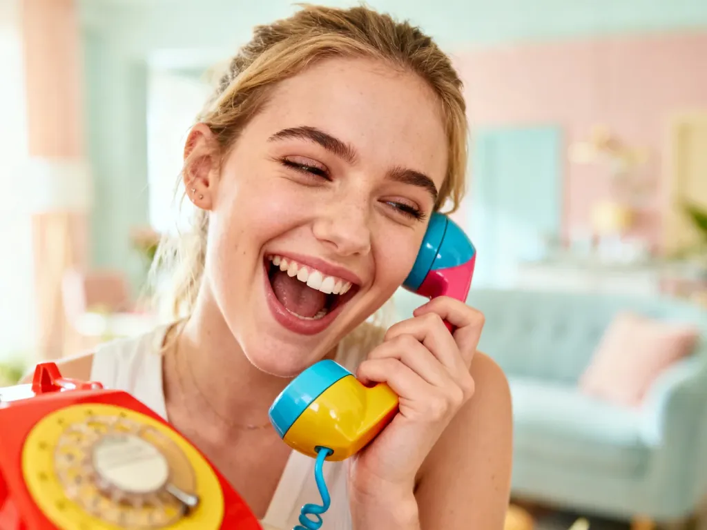 Młoda kobieta energicznie rozmawia przez kolorowy telefon w stylu vintage, obrazując ideę nieustannego gadania.